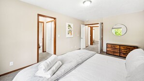 A bedroom with a large bed, a wooden dresser, and a door leading to another room.