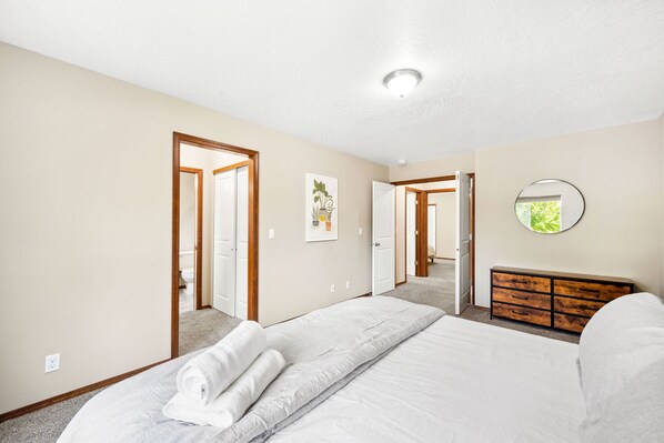 A bedroom with a large bed, a wooden dresser, and a door leading to another room.