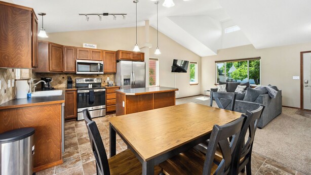 A modern kitchen with wooden cabinets, stainless steel appliances, and a dining area with a wooden table and chairs.