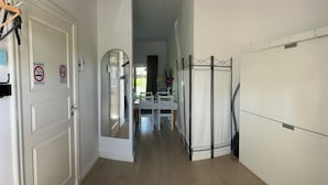 Un pasillo con una puerta blanca, un cartel de prohibido fumar, un espejo y un comedor con mesa y sillas.