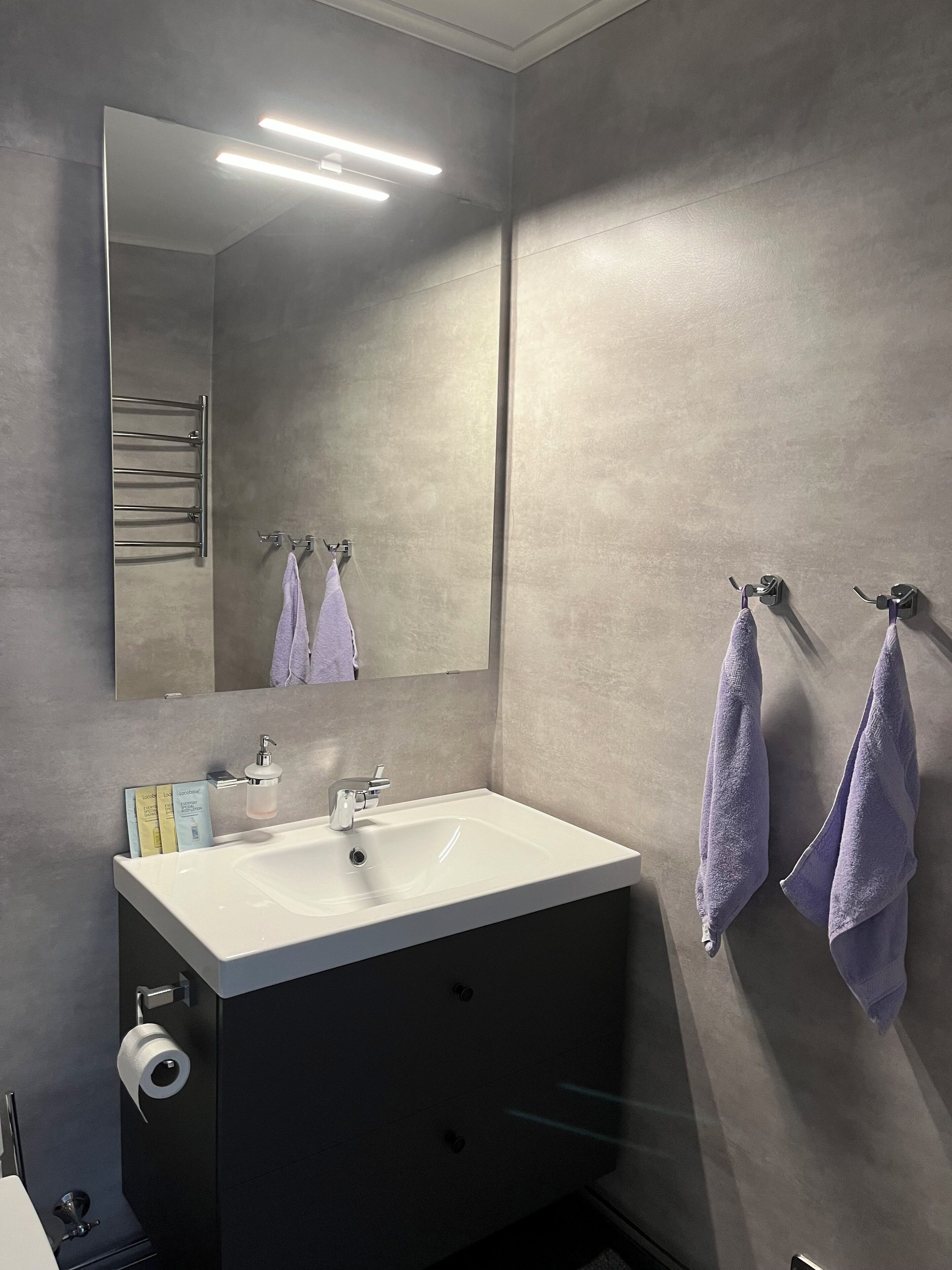 A modern bathroom with a large mirror, a white sink, and two towels hanging on towel racks.