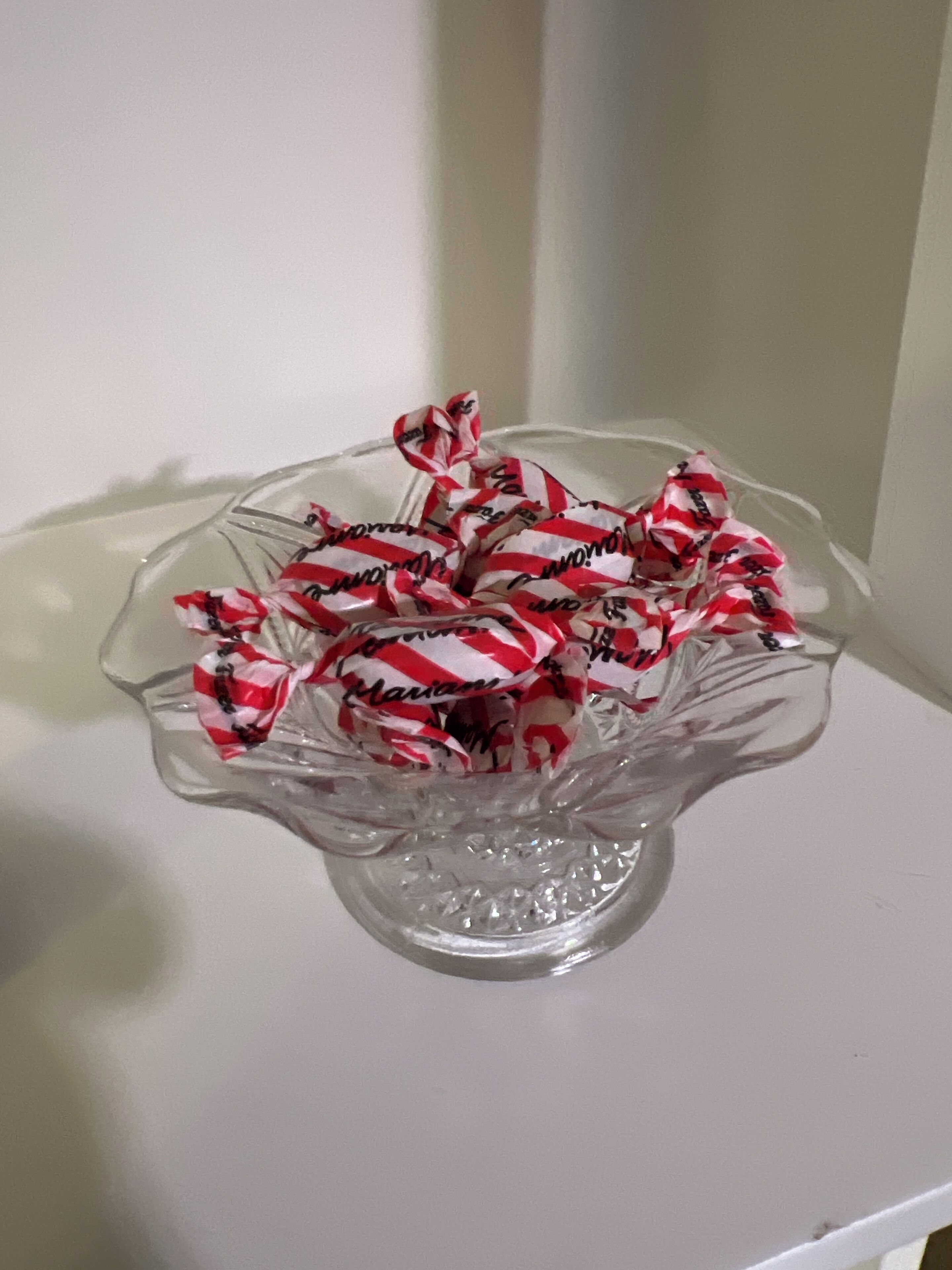 Un tazón de vidrio transparente lleno de envoltorios de caramelos a rayas rojas y blancas.