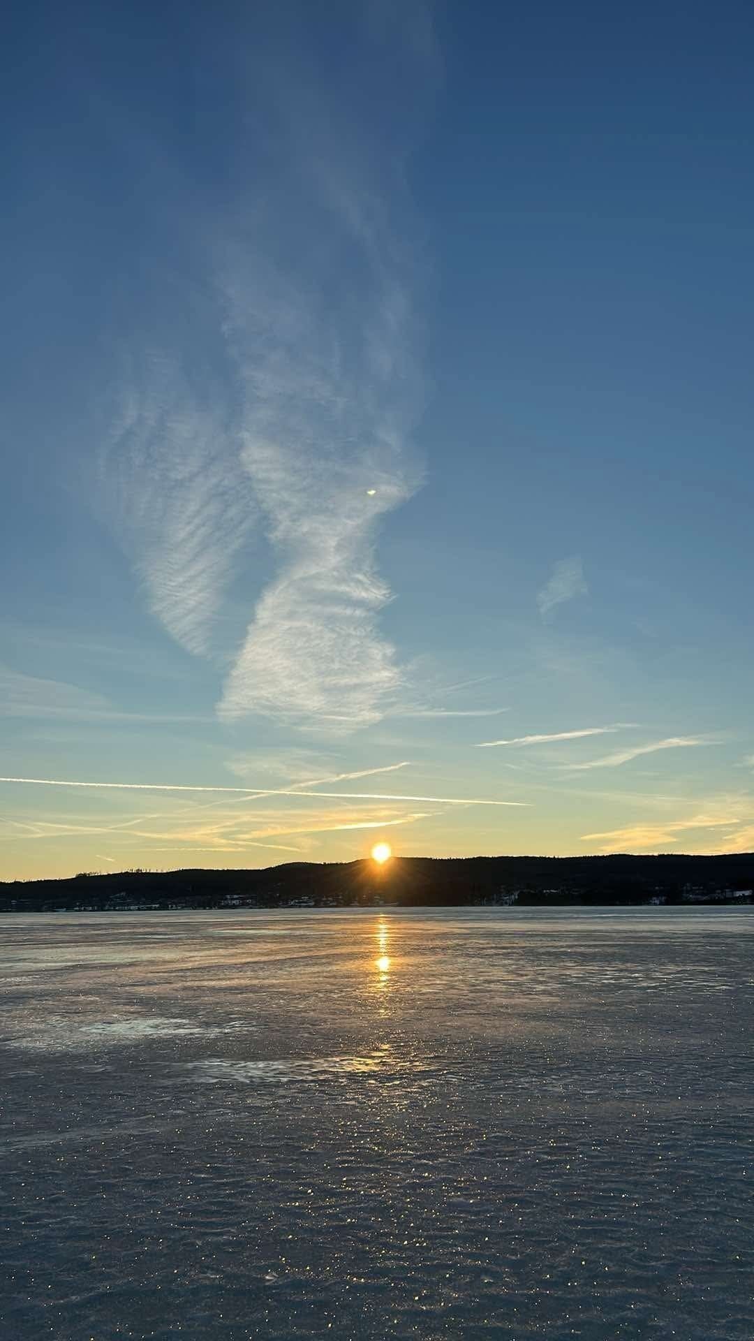 A frozen lake with the sun reflecting on the water's surface.