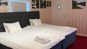 A hotel room with a large bed, a door with a round window, and a red carpet.