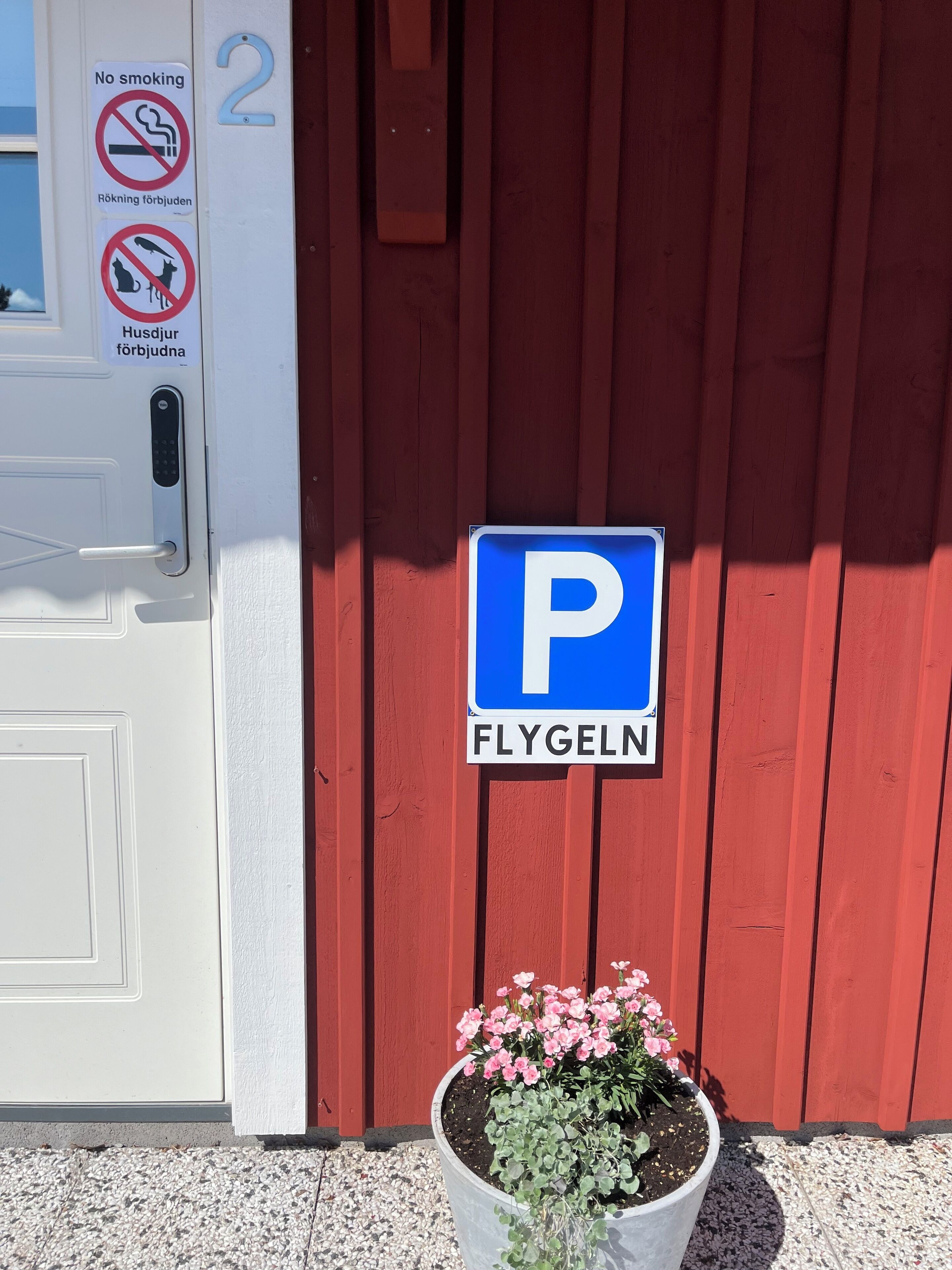 En röd byggnad med en vit dörr, en skylt som förbjuder rökning och en parkeringsskylt.