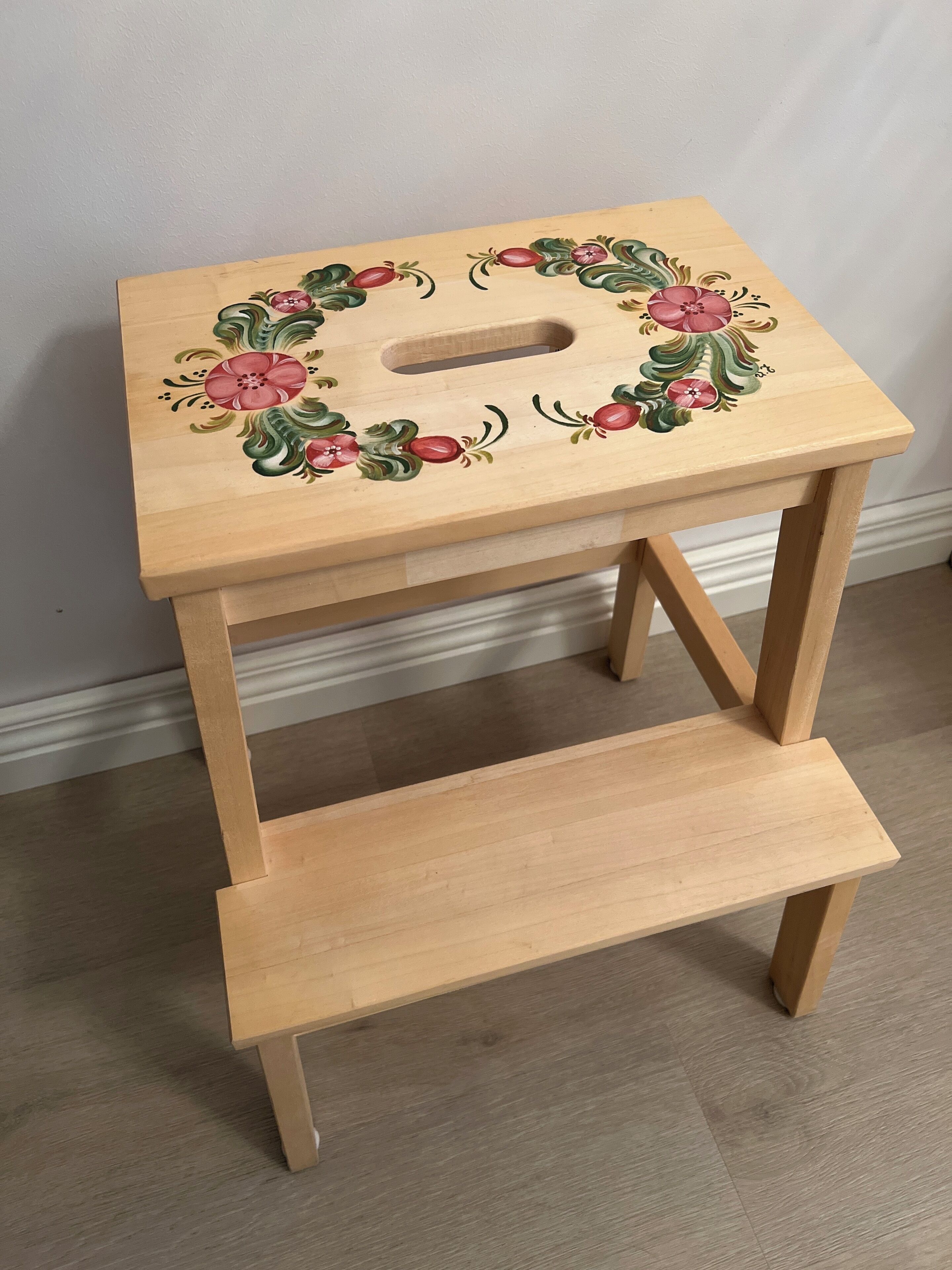 Un tabouret en bois orné d’un motif floral sur le dessus et doté d’une étagère inférieure.