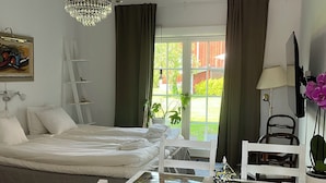 Un dormitorio con cama, lámpara de araña, ventana con cortinas, escritorio con sillas y un cuadro en la pared.