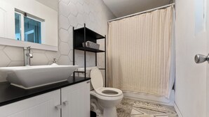 Een badkamer met een wit wastafelmeubel, een zwart aanrecht, een wit toilet en een douchegordijn.