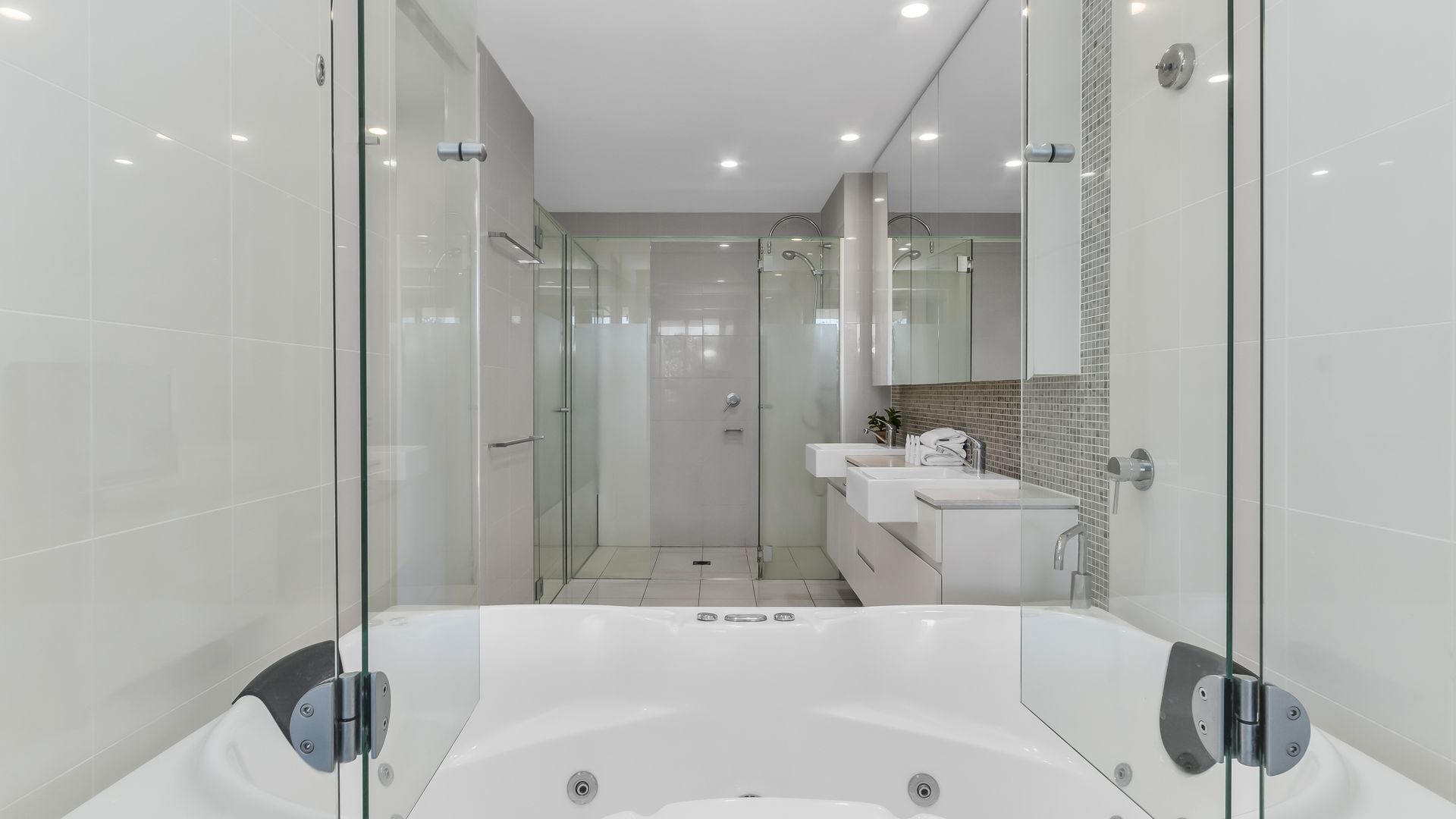 A modern bathroom with a glass-enclosed shower, a large bathtub, and a vanity with a mirror.
