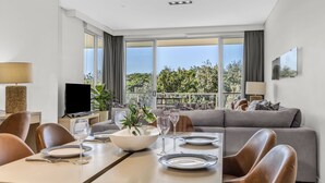 Uma sala de estar moderna com área de jantar, janelas amplas com vista e uma televisão de tela plana.
