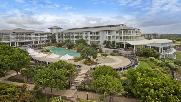 A resort with a central pool, multiple guest rooms, and lush landscaping.