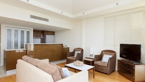 A compact living space with a sofa, two armchairs, a coffee table, a TV, and a kitchenette in the background.