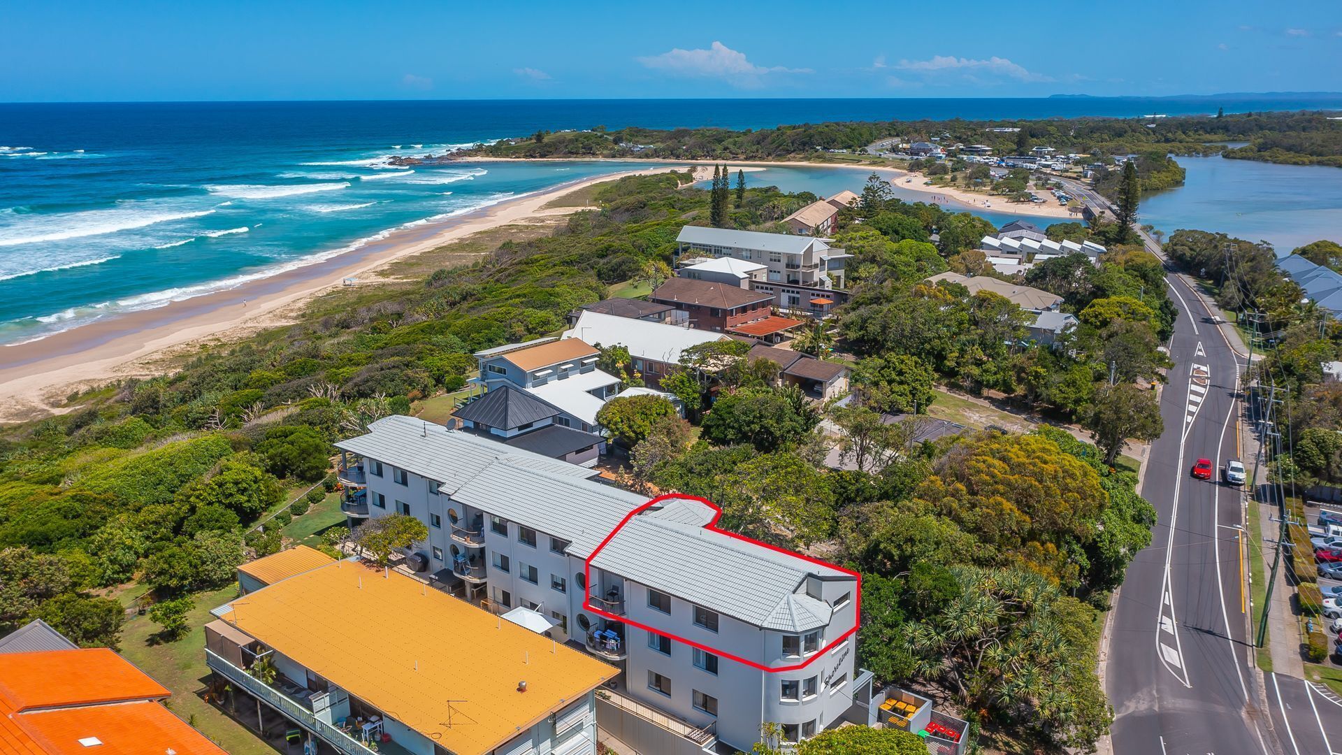 An aerial view of a coastal residential area with houses, a beach, and a road.