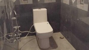 A bathroom with a toilet, a shower, and patterned tiles on the walls. - The Nirmala palace (Faizabad)