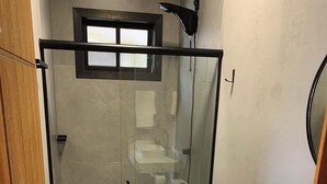 Casa de banho com chuveiro envidraçado, sanita e lavatório.