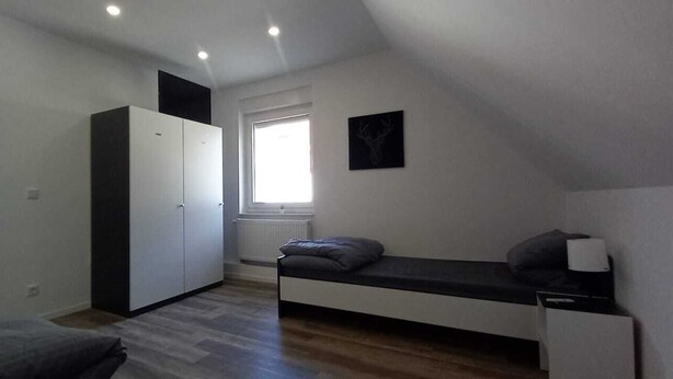A small, well-lit room with a bed, a wardrobe, and a window providing natural light. - Monteurzimmer mit Fast Wlan, Einzelbetten, Smart TV je Zimmer, Osnabrück (Osnabrück)