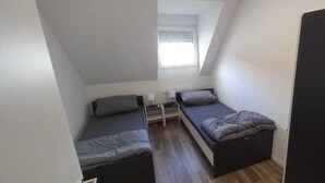 A small, compact room with two single beds, a window with blinds, and a radiator. - Monteurzimmer mit Fast Wlan, Einzelbetten, Smart TV je Zimmer, Osnabrück (Osnabrück)