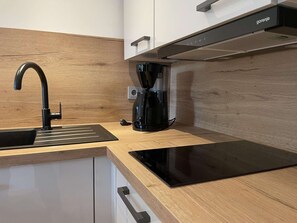 A modern kitchen with a black faucet, a coffee maker, and a black induction cooktop. - Designer-fewo in der Nähe zum Südstrand (Borkum)