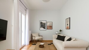 A modern living room with a sofa, a coffee table, and a chair. There are two framed artworks on the wall.