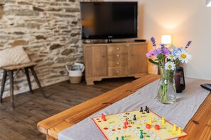 Une table en bois avec un jeu de société, un vase rempli de fleurs et un téléviseur dans une pièce aux murs en pierre.