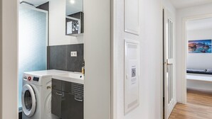 A laundry area with a washing machine, a drying rack, and a mirror. There is a door leading to a bedroom with a bed and a painting on the wall. - Apartment 'Wohnung 03' with Balcony and Wi-Fi (Waiblingen)