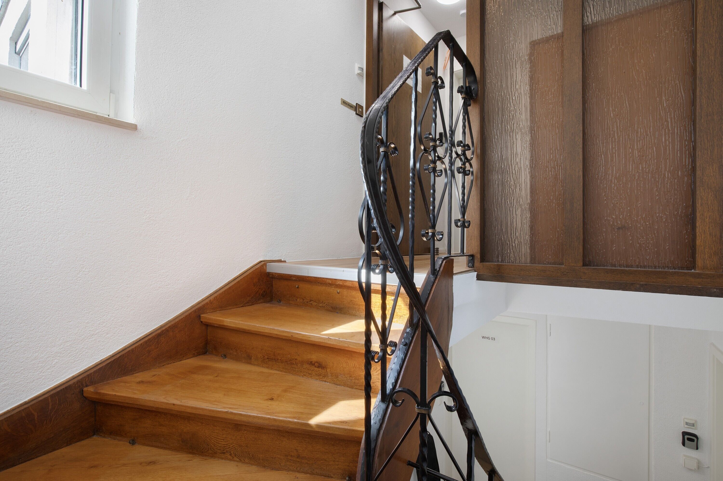 A wooden staircase with a metal railing, white walls, and a wooden door.