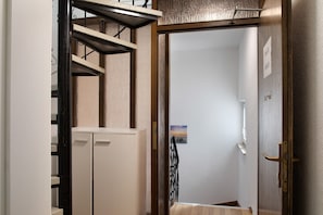 Un couloir avec un escalier en bois, une porte dotée d’une poignée en laiton et un tableau accroché au mur.