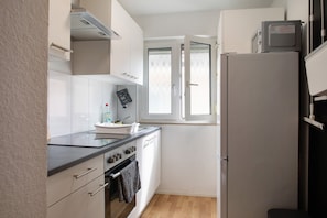 Une cuisine de taille réduite avec des meubles blancs, un plan de travail noir, une cuisinière et un réfrigérateur.