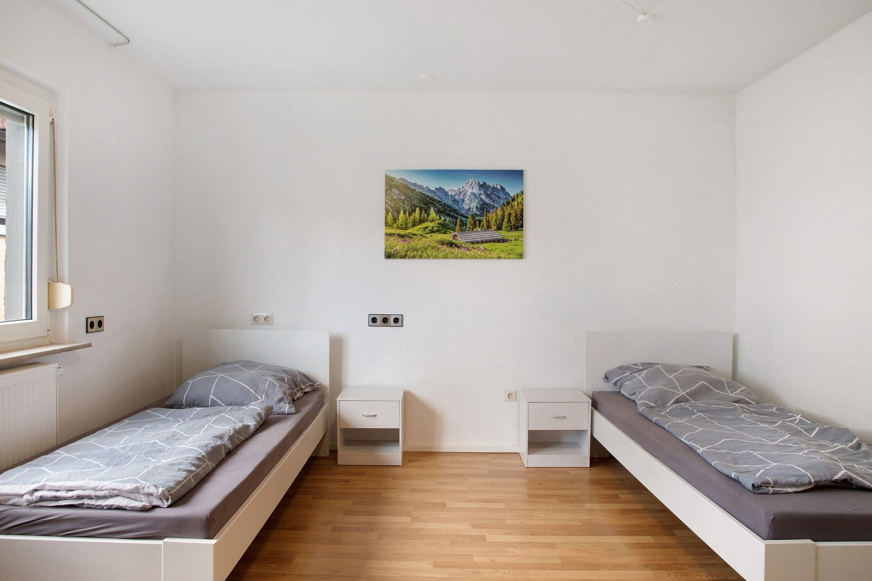 Una camera da letto con due letti singoli, pavimento in legno, una finestra e un dipinto con paesaggio montano.