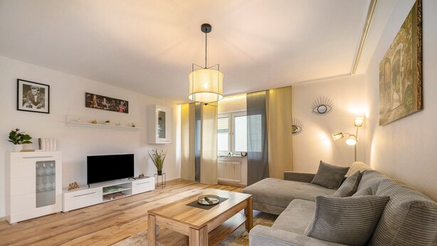 A living room with a wooden coffee table, a sofa, a TV, and a ceiling light fixture. - Apartment 'Neue 4 Zi Küche Bad Parknähe' with Balcony and Wi-Fi (Neunkirchen)