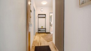 A hallway with a wooden floor, a small table with a plant, a mirror, and a wall-mounted light fixture. - Apartment 'Neue 4 Zi Küche Bad Parknähe' with Balcony and Wi-Fi (Neunkirchen)