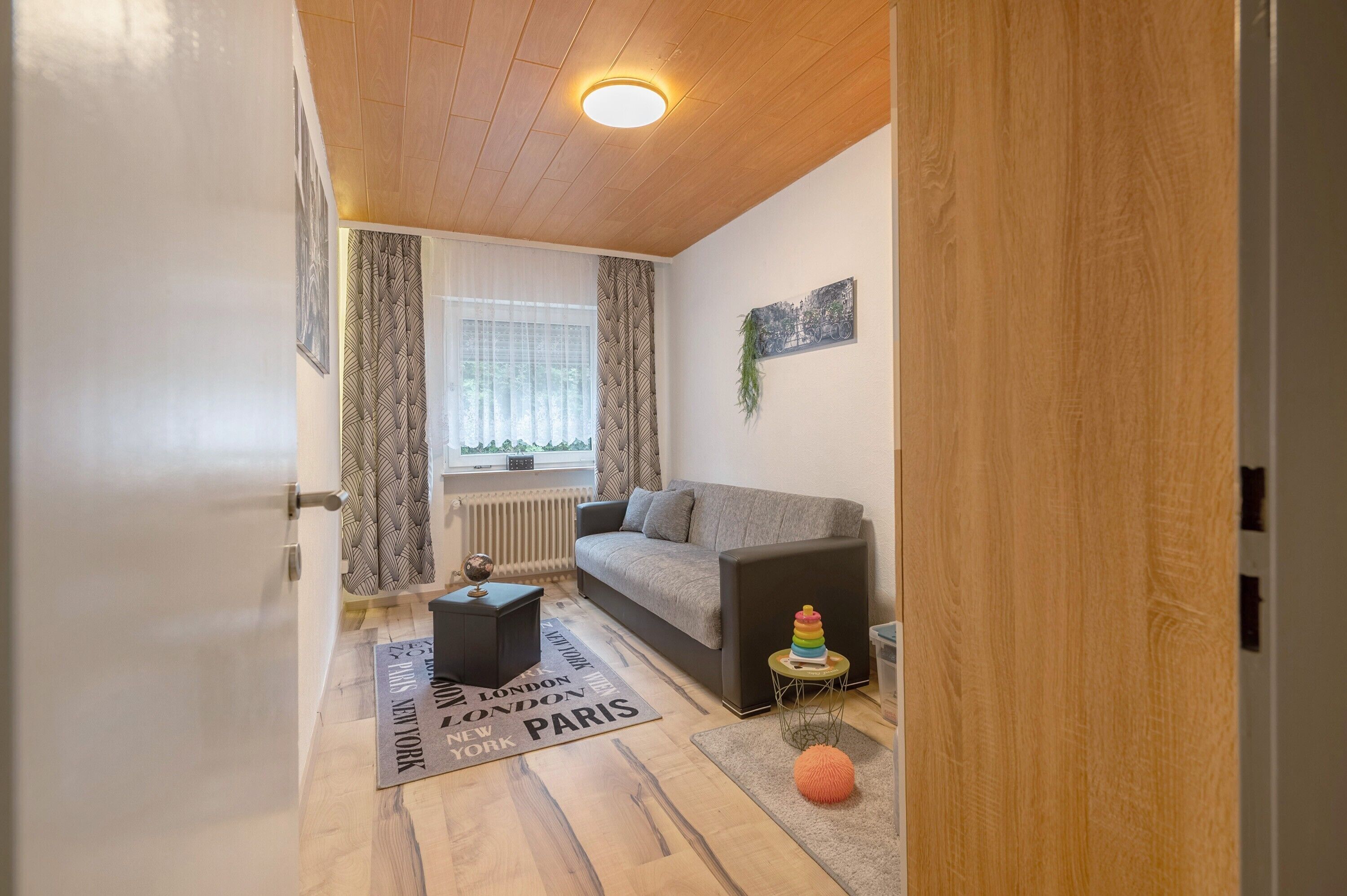 Un salón con sofá, una mesita, un radiador y una ventana con cortinas.