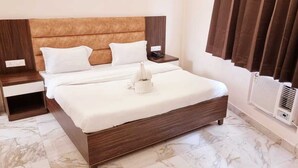 Una cama bien hecha con sábanas blancas y una almohada decorativa, una mesita de noche con lámpara y un aire acondicionado instalado en la pared.