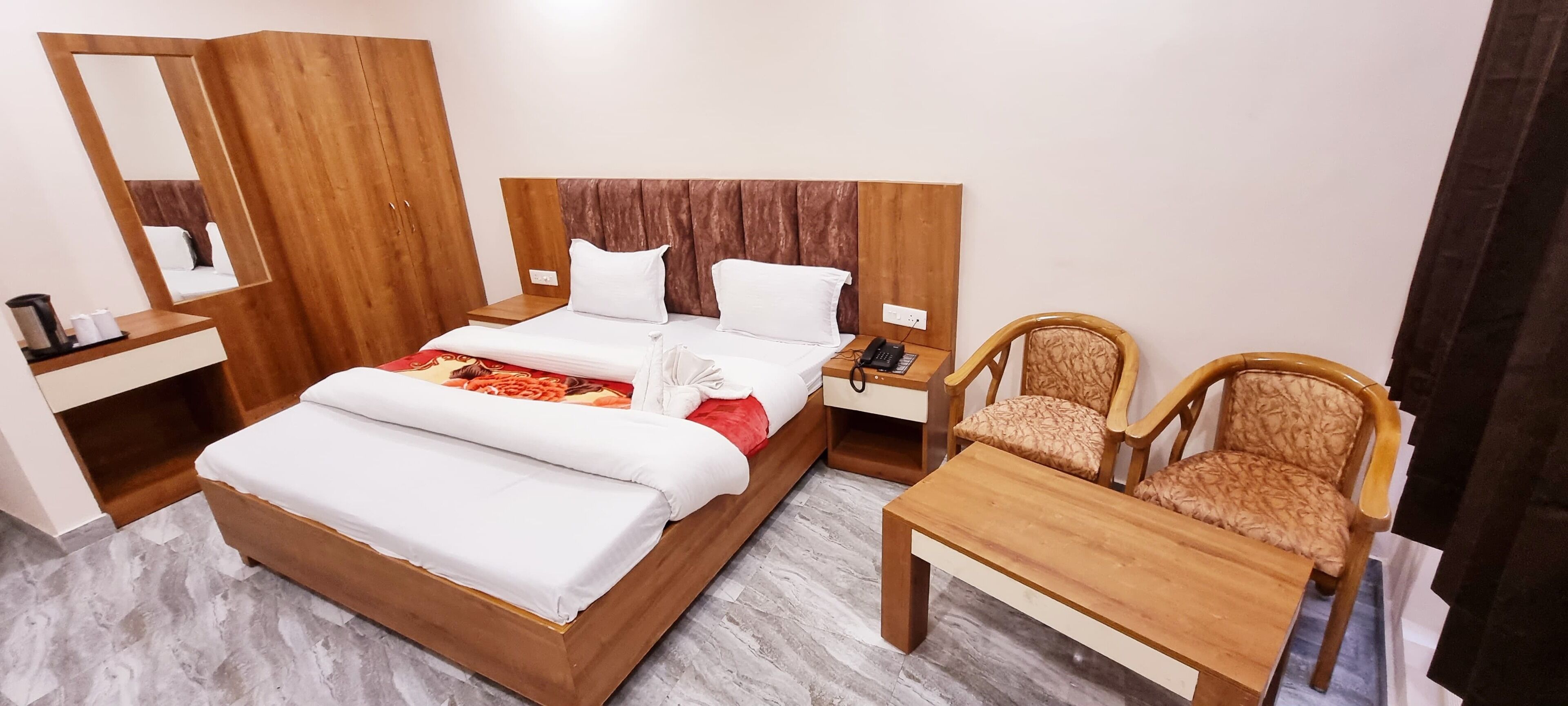 Una habitación de hotel con una cama de madera, una mesita de noche con un teléfono, dos sillas, una pequeña mesa y un espejo.