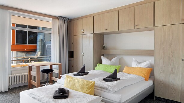 Quarto de hotel com duas camas, uma escrivaninha e vista para o exterior.