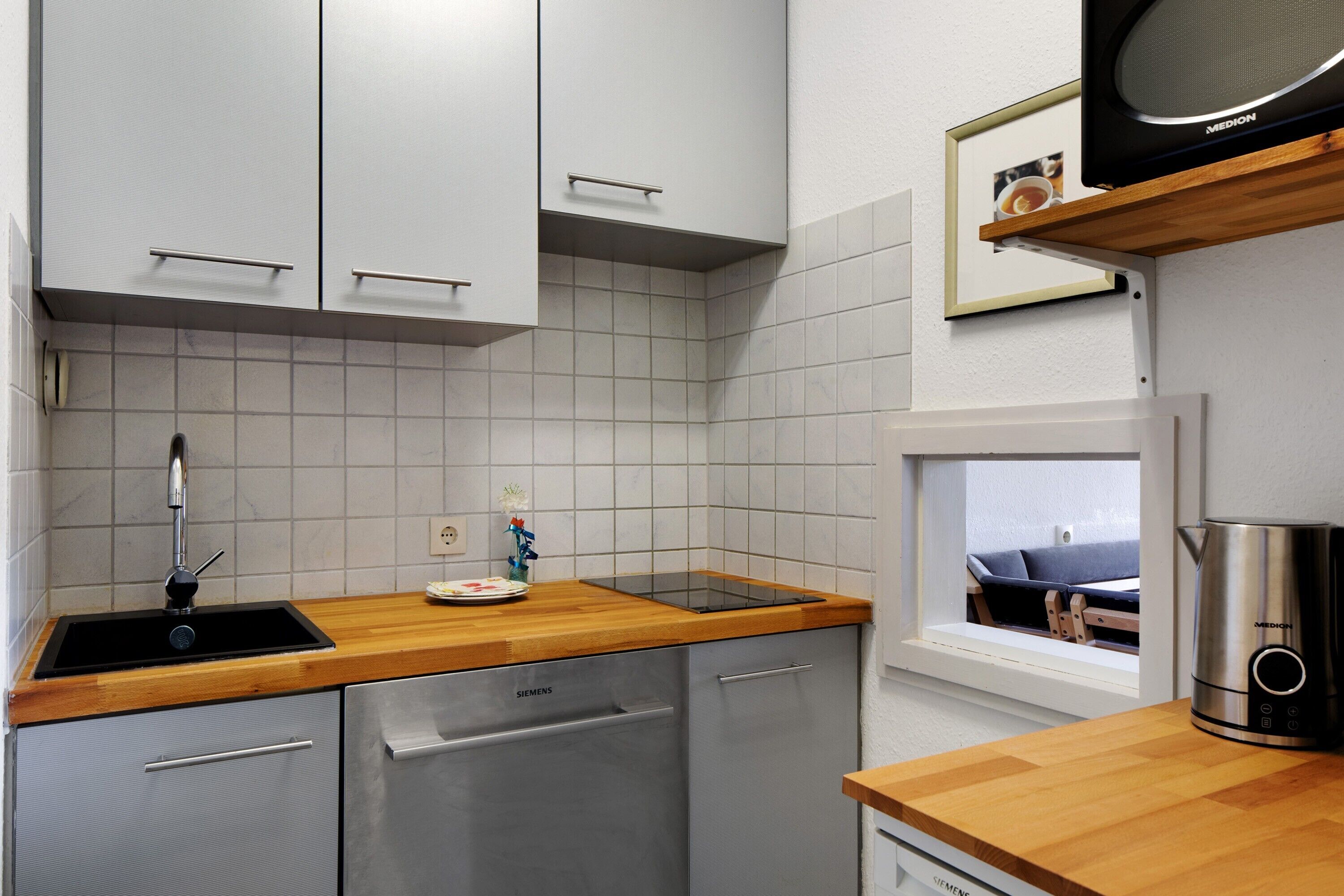 Une cuisine moderne avec des meubles blancs, un plan de travail en bois, un lave-vaisselle et une fenêtre donnant sur un beau paysage.