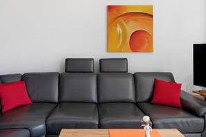 Un canapé en cuir noir avec des coussins rouges, une table basse en bois et un tableau accroché au mur.