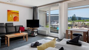 Uma sala de estar moderna com sofá, mesa de centro, TV e uma grande janela com vista para o exterior.