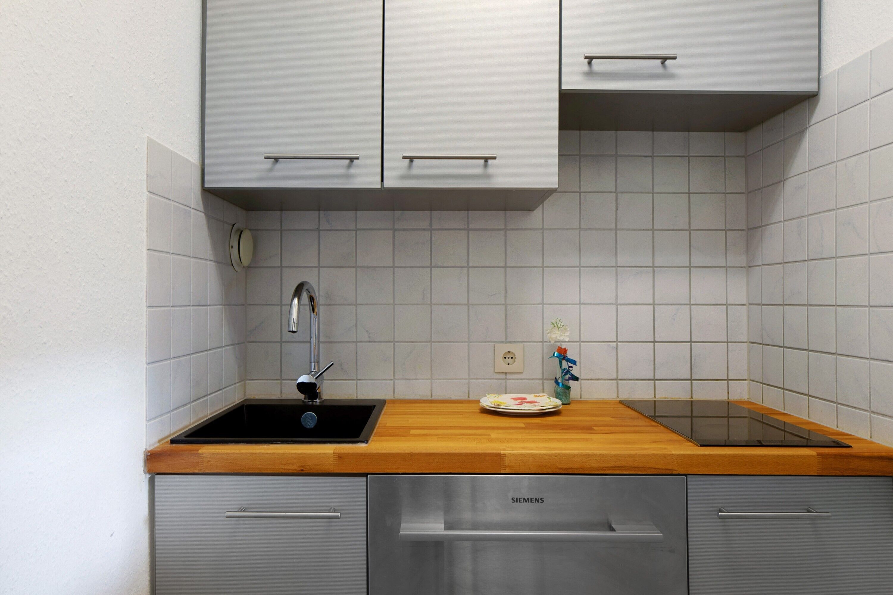 Una cocina con encimera de madera, electrodomésticos de acero inoxidable y paredes de azulejos blancos.