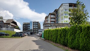 Um edifício residencial com vários andares, varandas, área de estacionamento e um hedge bem cuidado.