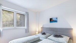 Una habitación con dos camas, una ventana con cortinas, un cuadro en la pared y una lámpara de noche.