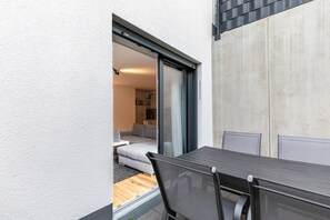 Een moderne buiten eethoek met een tafel en stoelen, een schuifpui naar een leefruimte en een betonnen muur.