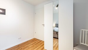 Una habitación con piso de madera, paredes blancas, un armario blanco y una silla blanca.