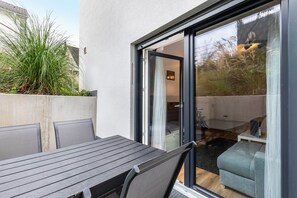 Een terras met een tafel en stoelen, een schuifdeur en uitzicht op het interieur.