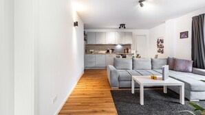 Una sala de estar moderna con un sofá gris, una mesa de centro blanca y una cocina al fondo.