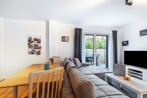 Un salon moderne comprenant un canapé, une table à manger, un téléviseur et un balcon agrémenté de rideaux.