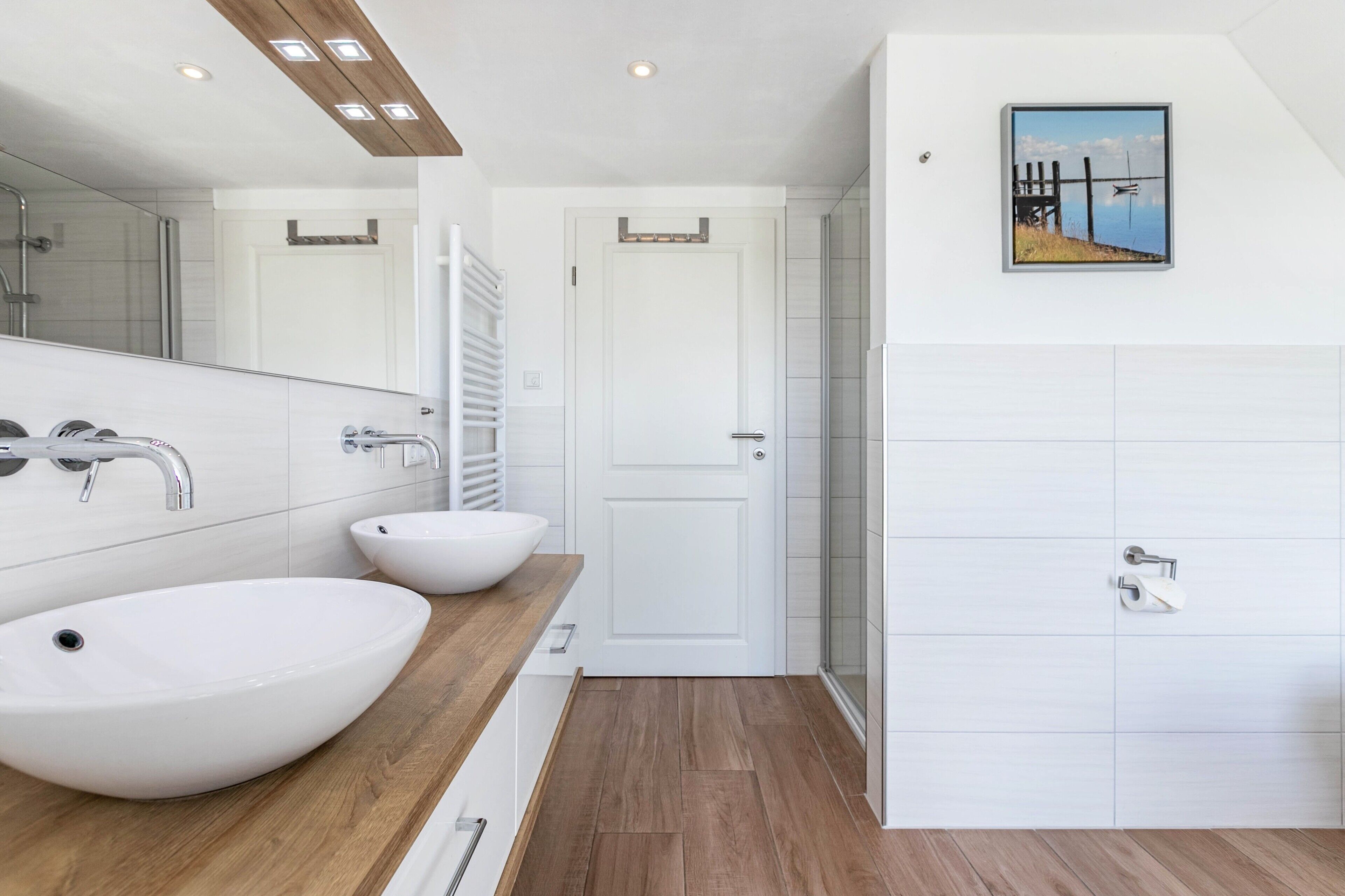 A modern bathroom with two large white sinks, a mirror, and a framed picture on the wall.