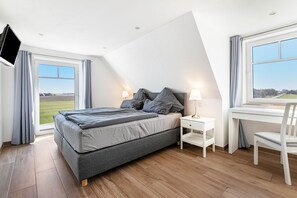 Una camera da letto con un letto, comodini, una scrivania, una sedia, una TV e ampie finestre con tende.