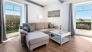 Ein modernes Wohnzimmer mit einem Ecksofa, einem Glastisch und großen Fenstern mit Blick ins Freie.