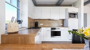 Cozinha moderna com armários brancos, forno de aço inoxidável, micro-ondas e bancada de madeira.